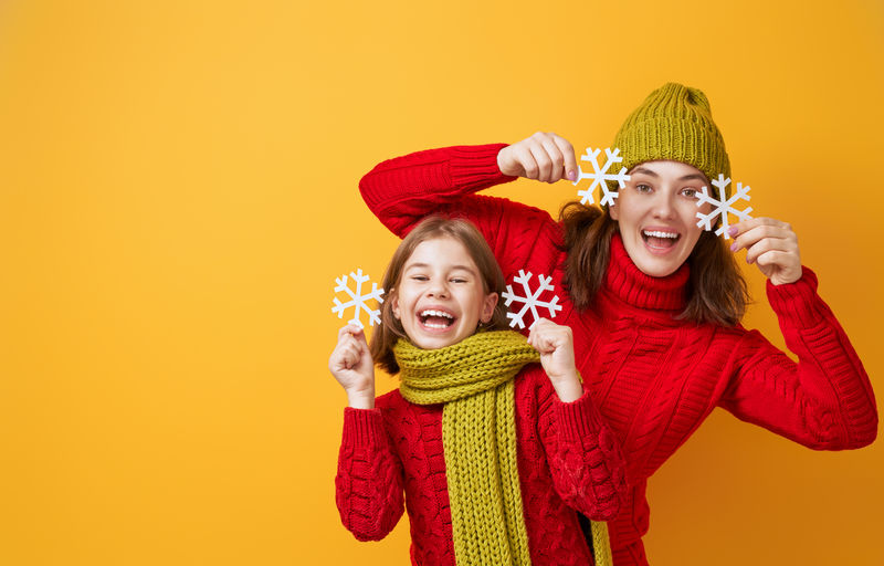 一个幸福的家庭的冬季肖像-戴着针织帽子-鼻子和毛衣-母子俩在黄色背景下嬉戏嬉笑-时尚概念
