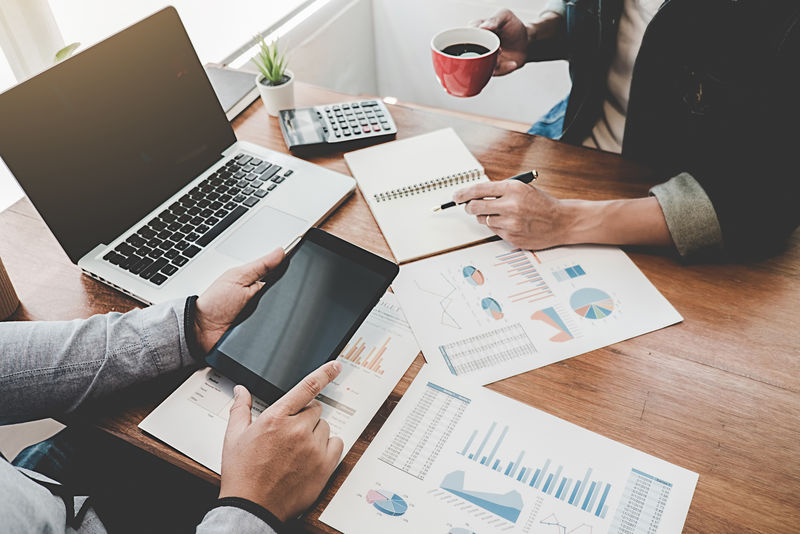 年轻人在咖啡店工作-使用笔记本电脑-手持智能手机-讨论显示他们成功团队合作成果的图表