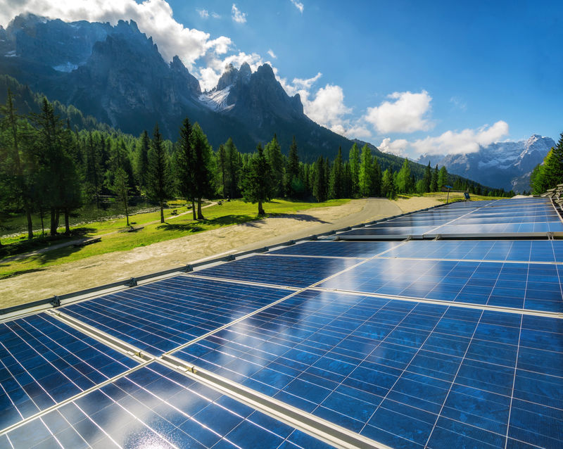 阳光明媚的天空和山脉背景下的乡村景观中的太阳能电池板-太阳能是世界能源可持续发展的创新-可持续资源