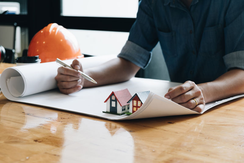 杨建文用蓝图和小房子模型安全盔和咖啡杯-杨建工在建筑规划项目工作场所检查-绘制施工图