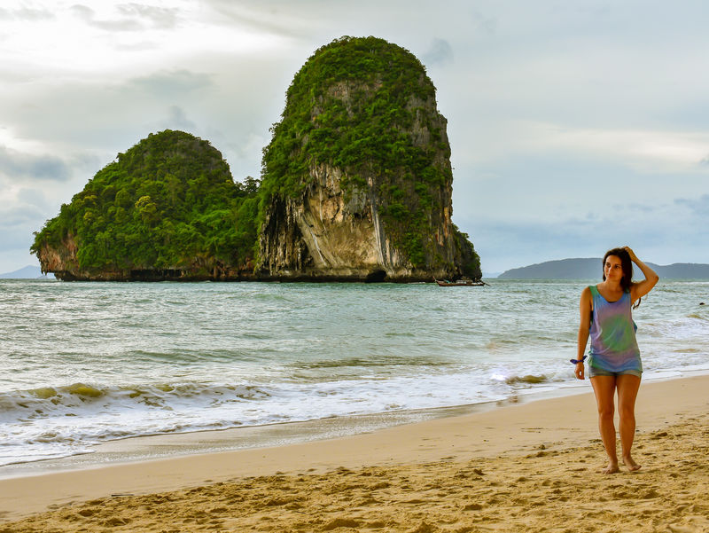 站在绿色和棕色岩层附近海滨的女人