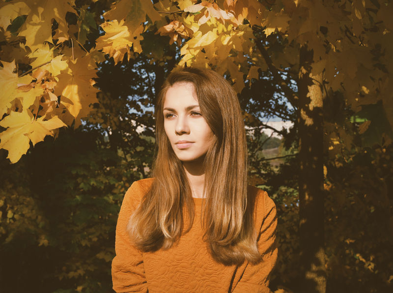 穿着橙色衬衫的女人站在树叶旁边