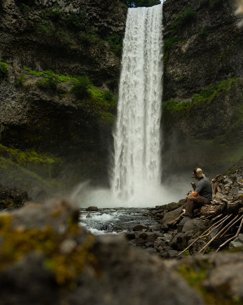 白天穿着黑衬衫的男人坐在瀑布附近的岩石上