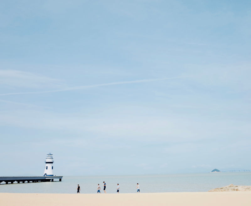 人们走过灯塔附近的海滩