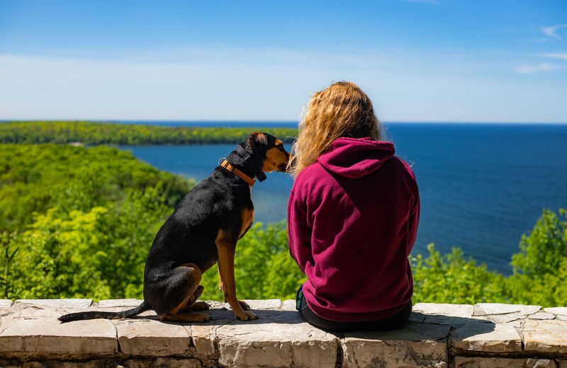 坐在狗旁边的女人面对着蓝色的水体