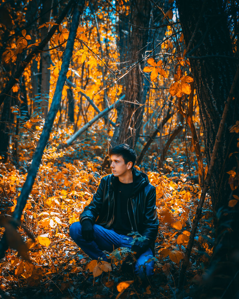 白天穿着黑色连帽衫和蓝色裤子的男人坐在树边