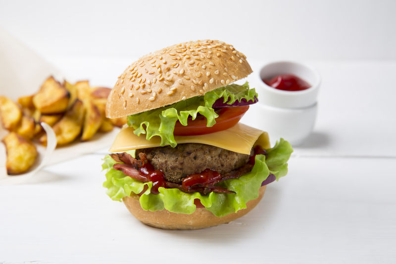 新鲜的自制汉堡，肉、番茄酱和炸薯条放在浅色木质背景上。复制空间。