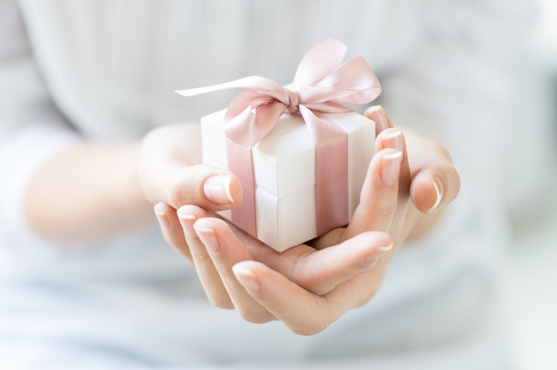 女性手拿着一个用粉色丝带包裹的小礼物的特写镜头-室内女性手中的小礼物-聚焦在小盒子上的浅景深