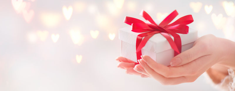 情人节礼物-美女手拿礼品盒-红色蝴蝶结的节日背景下-发光的心bokeh-特写-柔和的颜色-广角格式背景