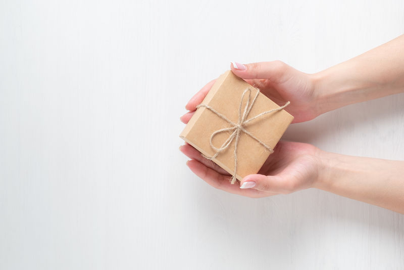 一个年轻女孩的手在白色的木制背景上打开一个礼品盒