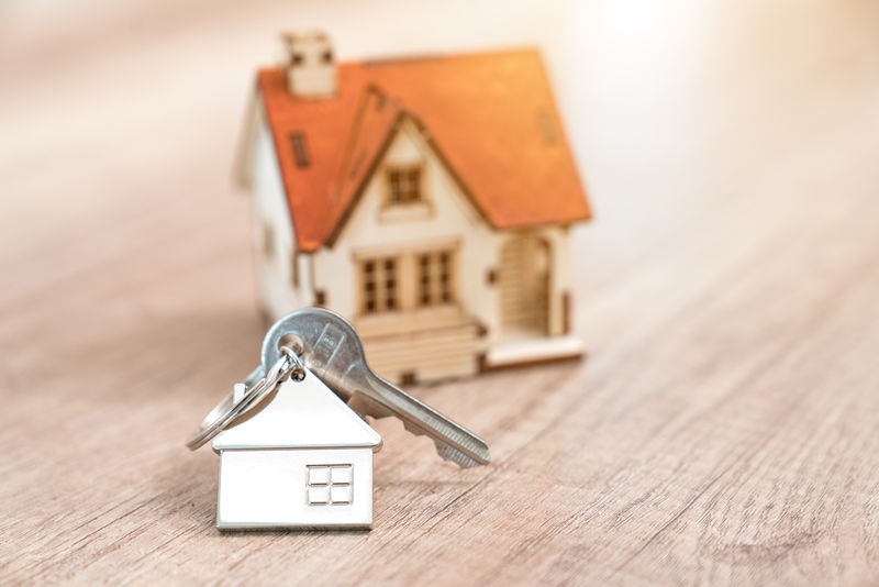 房子钥匙在一个房子形状的钥匙链搁置在木地板上的概念为不动产-搬家或租赁财产