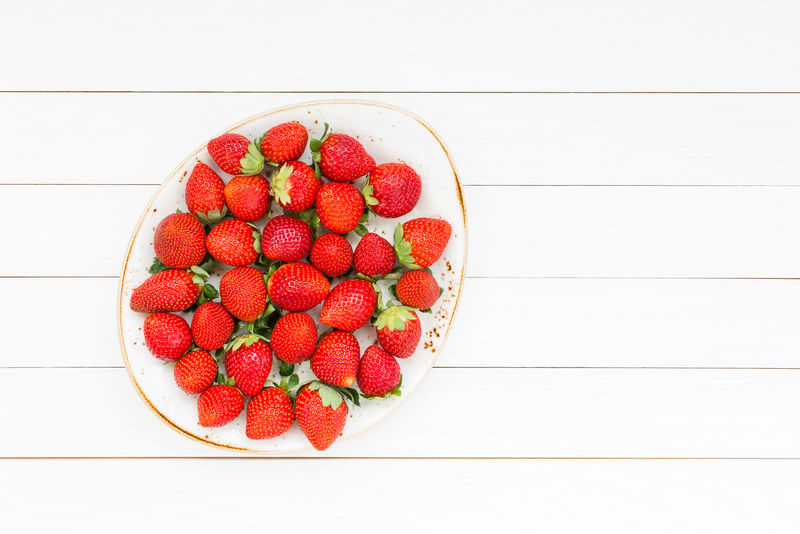 新鲜草莓盘在白色木桌上。俯视图