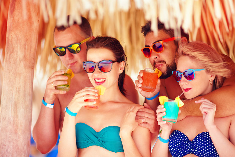 一群快乐的朋友在热带海滩上玩得开心，喝着五颜六色的鸡尾酒