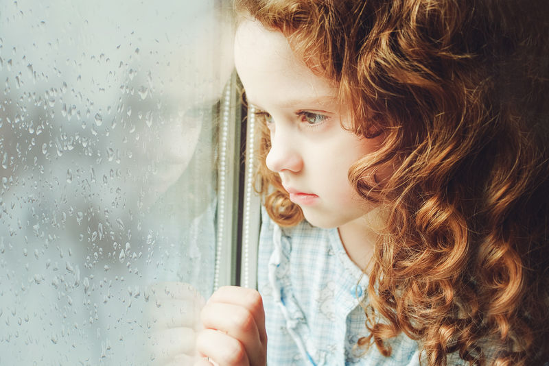 一个悲伤的孩子望着窗外的画像。调色照片。