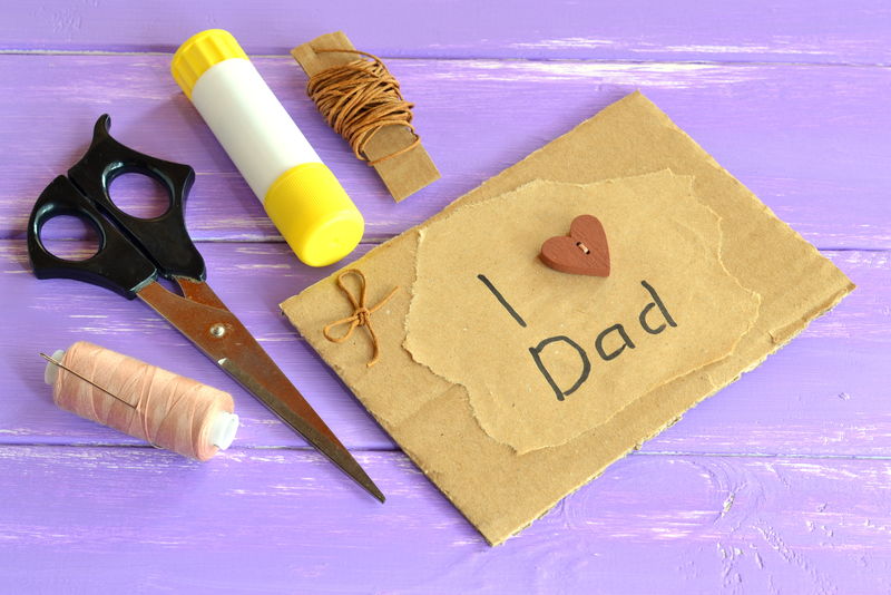 手拿贺卡，上面写着“我爱爸爸”。剪刀，胶水，绳子，线，针。孩子们的手工艺灵感。
