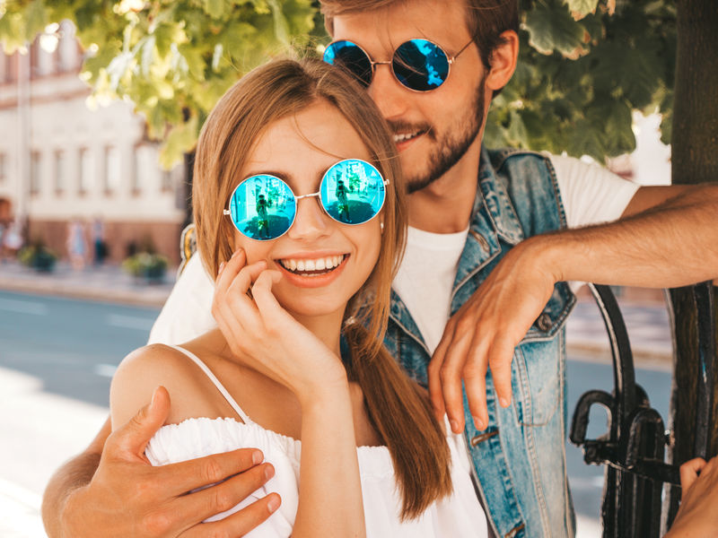 微笑的漂亮女孩和她英俊的男朋友。穿休闲夏装的女人和穿牛仔裤的男人。幸福快乐的家庭。在街上玩得开心的女性。戴着太阳镜拥抱情侣