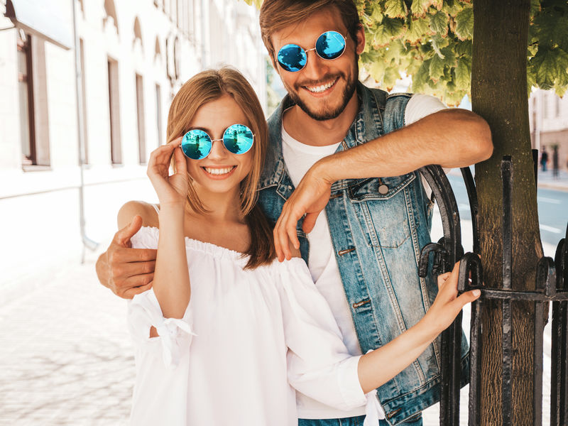 微笑的漂亮女孩和她英俊的男朋友。穿休闲夏装的女人和穿牛仔裤的男人。幸福快乐的家庭。在街上玩得开心的女性。戴着太阳镜拥抱情侣