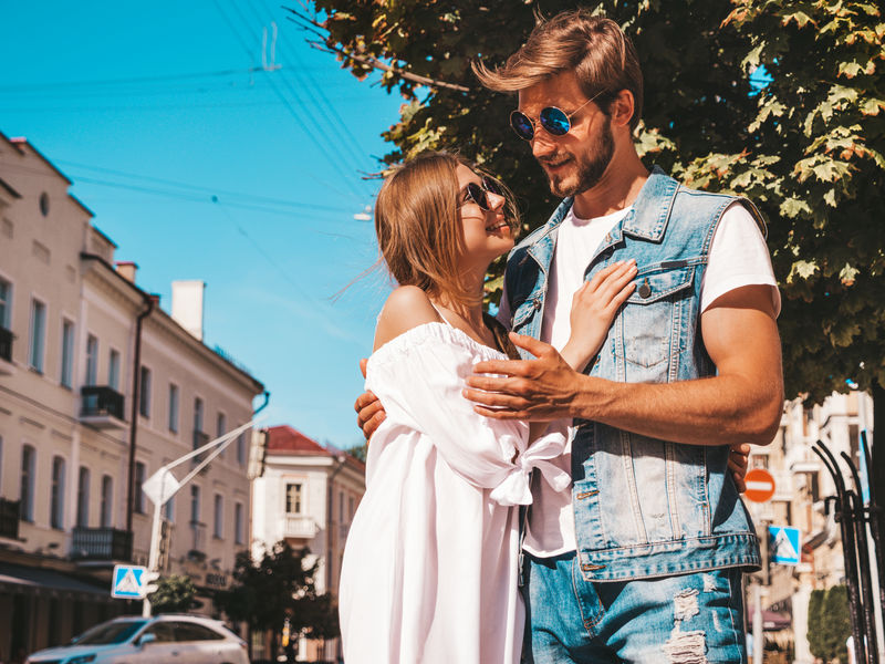 微笑的漂亮女孩和她英俊的男朋友。穿休闲夏装的女人和穿牛仔裤的男人。幸福快乐的家庭。在街上玩得开心的女性。戴着太阳镜拥抱情侣