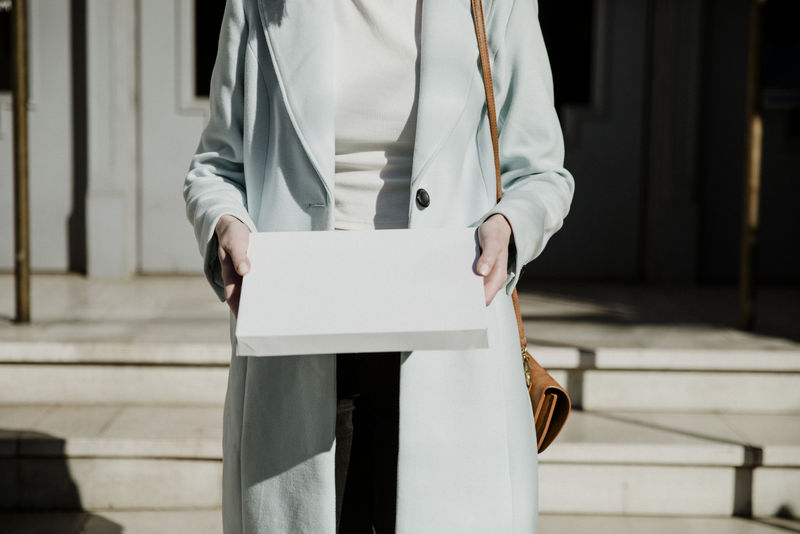 一个穿着大衣的女人拿着一个白色的盒子在一栋楼前