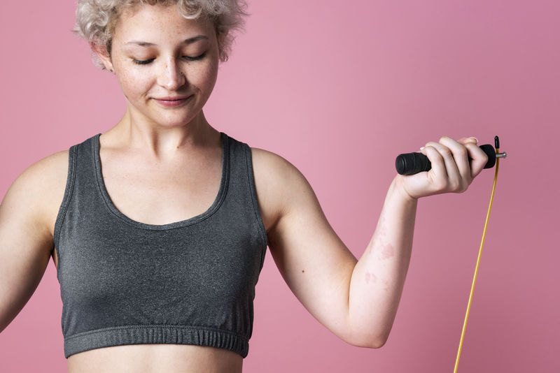 年轻活跃的女孩带着跳绳在粉色背景的工作室里进行有氧运动