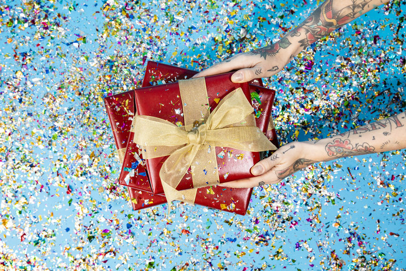 手上有纹身的手拿着五彩纸屑的红色礼盒