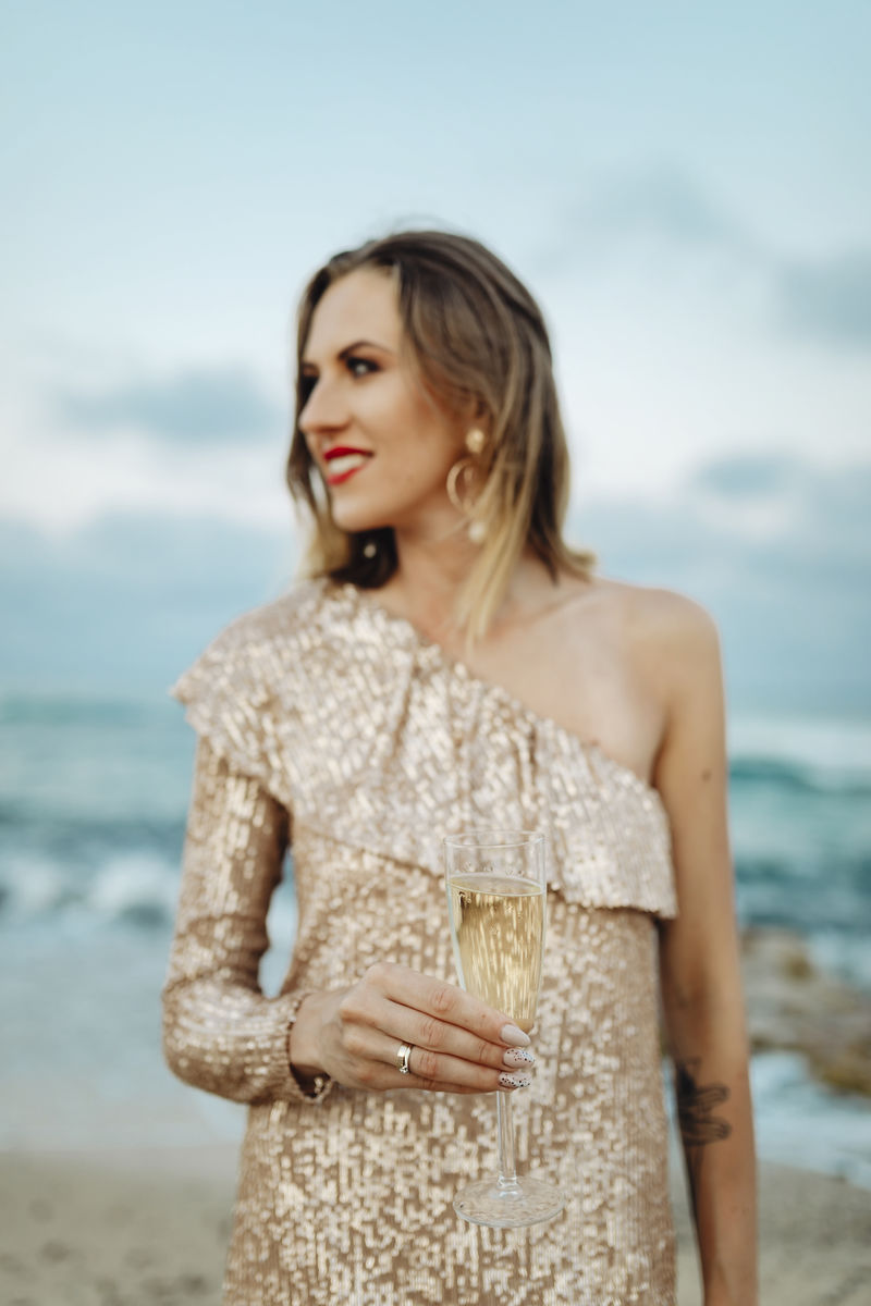 一个穿着金色裙子的女人在沙滩上喝着香槟