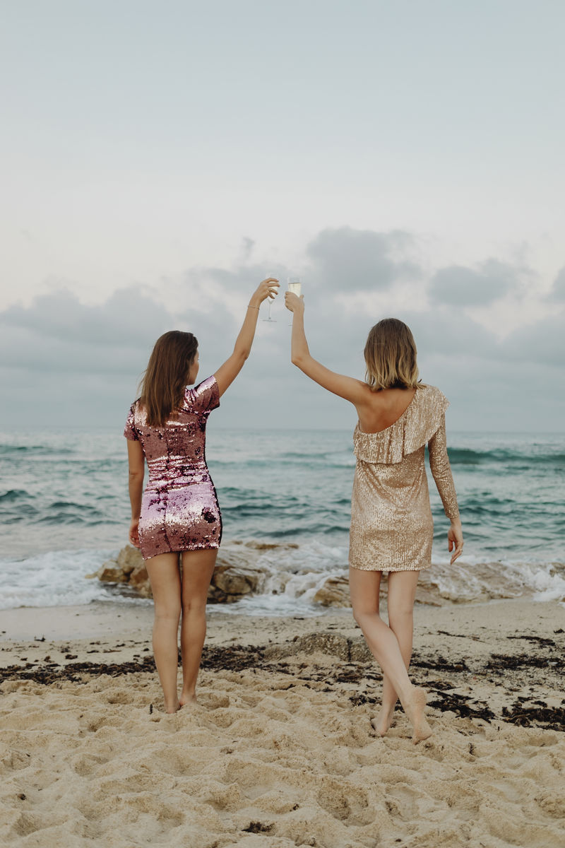 在海滩上碰杯香槟的女人的后视图