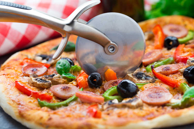 正在切割美味的香肠披萨