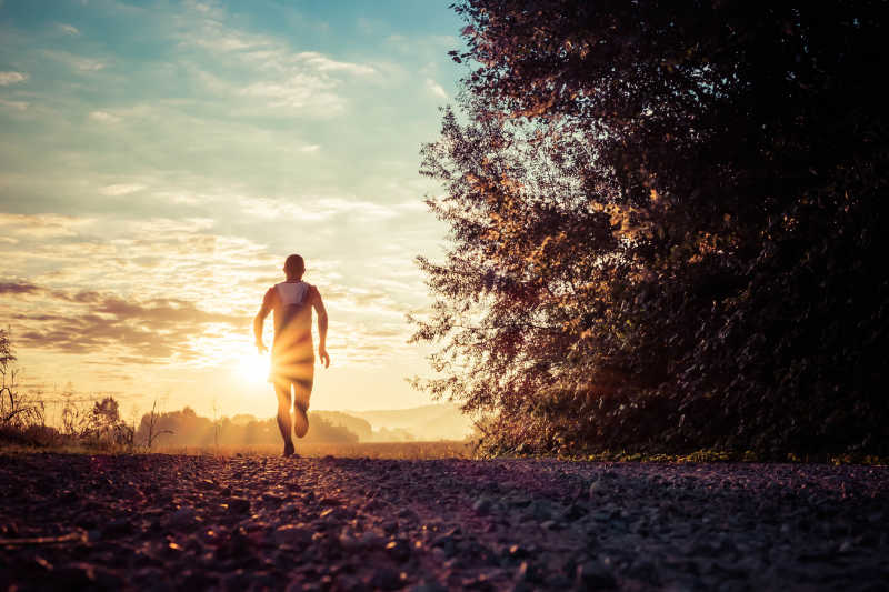 黎明阳光中在乡村路上跑步的男人