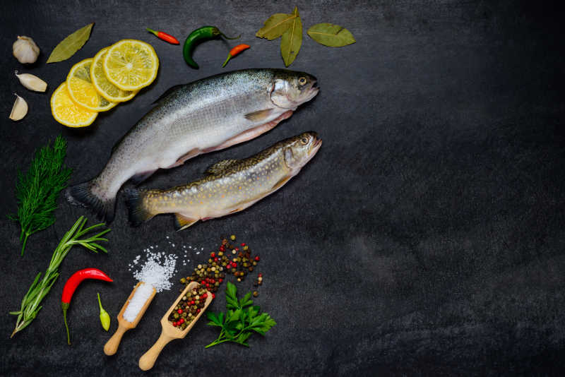 黑色案板上两条新鲜的鱼和做鱼所需配料