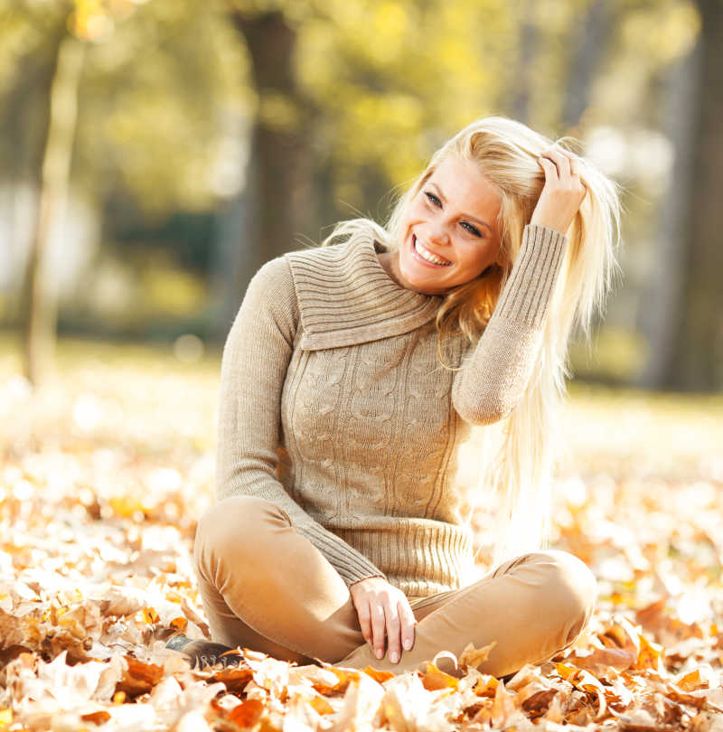美丽的金发女人在落叶上坐着微笑