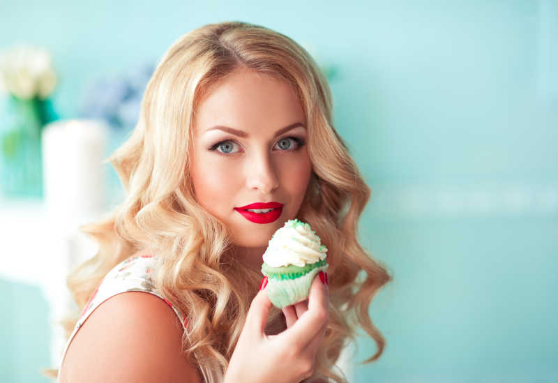 美丽的金发女郎在房间的壁橱里拿着杯子蛋糕