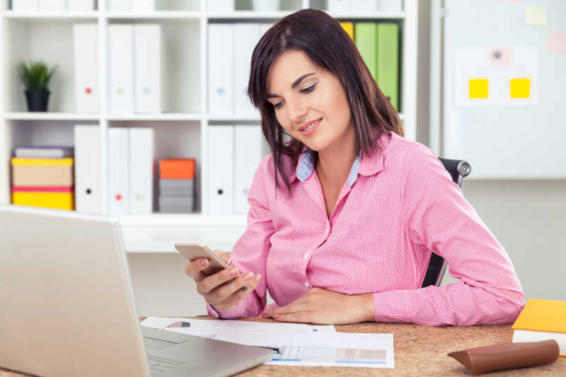 女商人坐在电脑前看手机