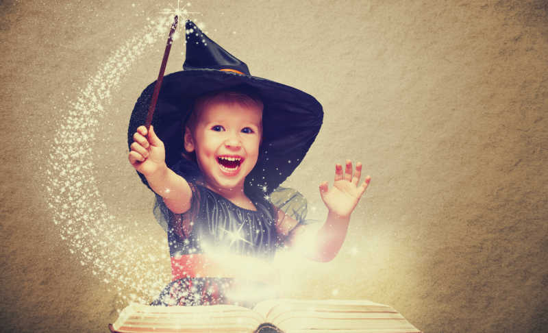 万圣节前夕的快乐的小巫婆用魔杖和发光的书变戏法和大笑