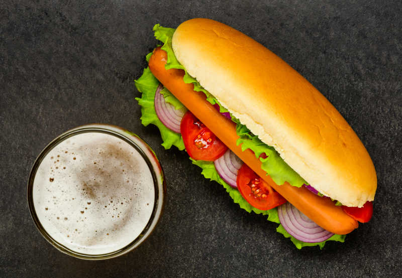 黑色背景图前的热狗配啤酒