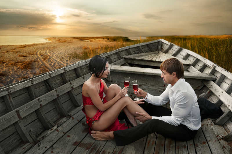 日落时在海边的旧船上的浪漫的情侣干杯