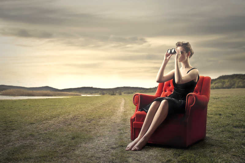 坐在红色沙发拿着望远镜看风景的女孩