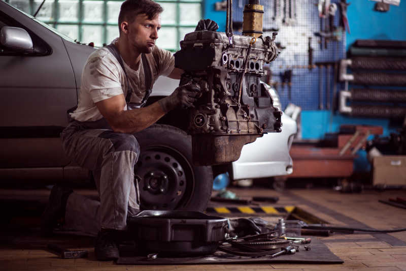 汽车修理厂力的拔出发动机的男性修理工