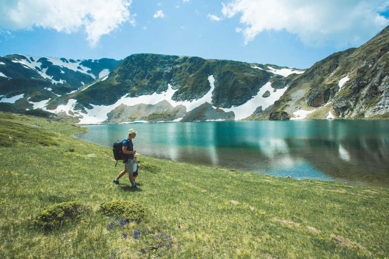 蓝天白云下带着儿子背着背包走在河边的男人
