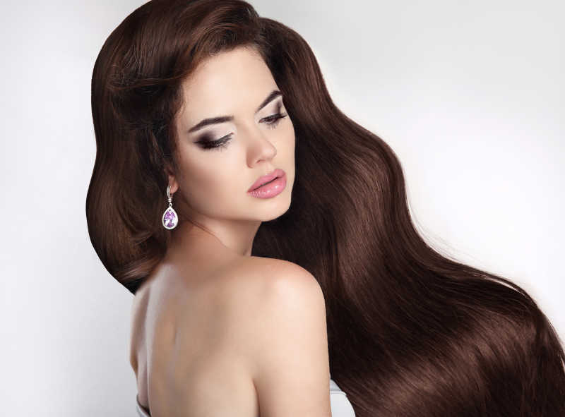 在工作室背景下的有着闪亮黑色波浪状头发的美丽的女子