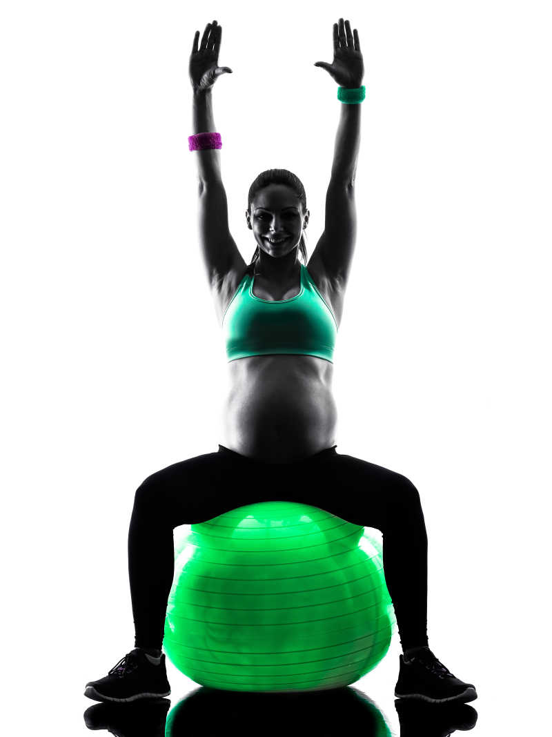 白色背景下坐在瑜伽球上健身锻炼的孕妇