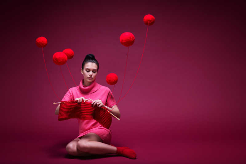 年轻的外国美女在用红色线球织毛衣