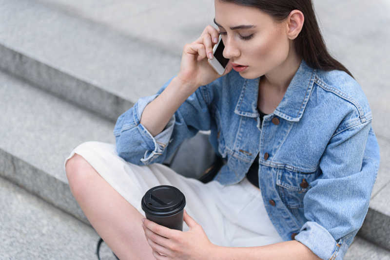 坐在台阶上拿着咖啡打电话的美女