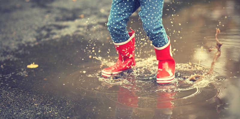 孩子穿着红色雨鞋在水坑玩耍