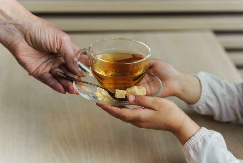 孩子从大人手中接过一杯茶和糖
