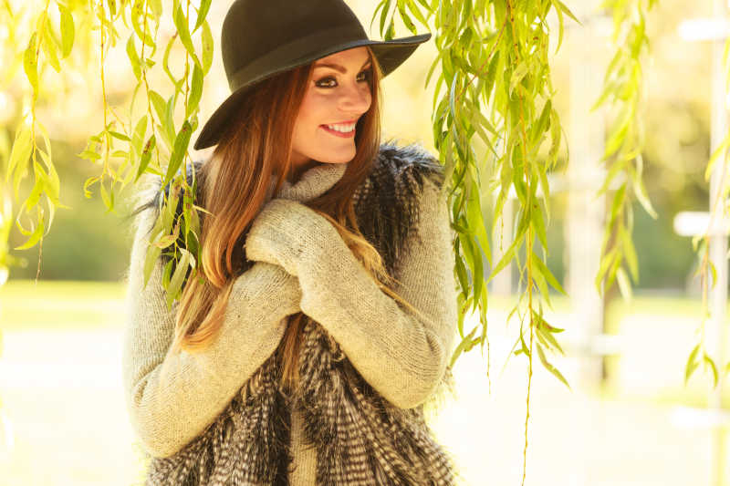 漂亮的年轻女子穿着时髦的毛衣和帽子温暖自己在户外