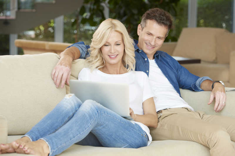 相拥的夫妻在沙发上看笔记本交谈着