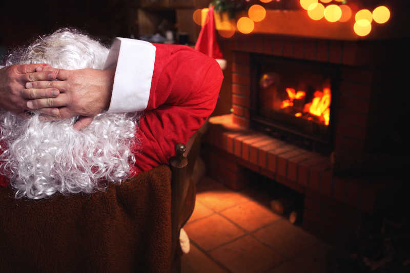 圣诞老人坐在燃烧的壁炉前的椅子上