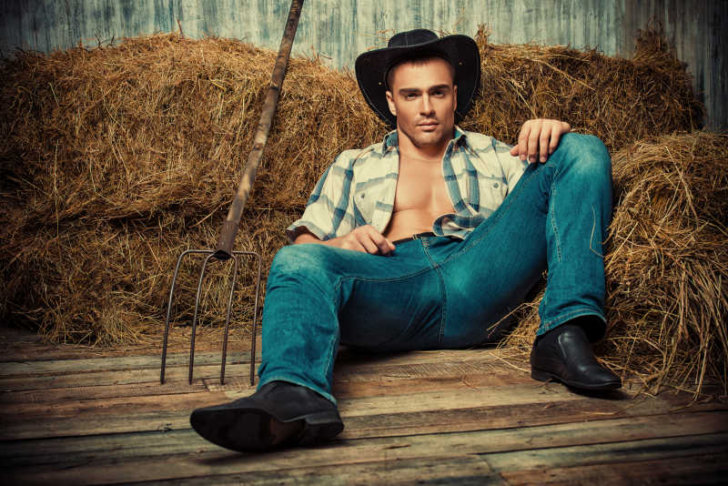 木板上半躺在草堆上的时尚男性模特