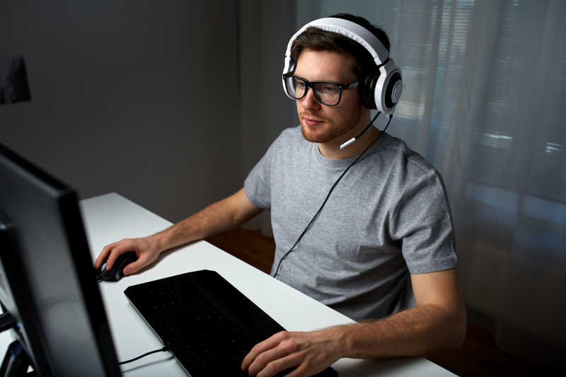 戴着耳机戴着眼镜在家玩电脑游戏的男人